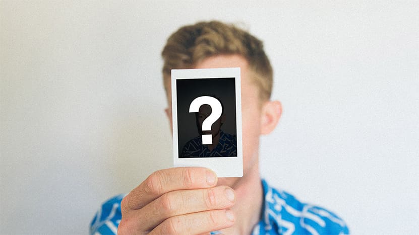 Man holding up a polaroid photo of a question mark covering his face